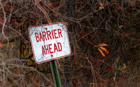 A selective focus shot of a barrier ahead sign leaned against a metal fence