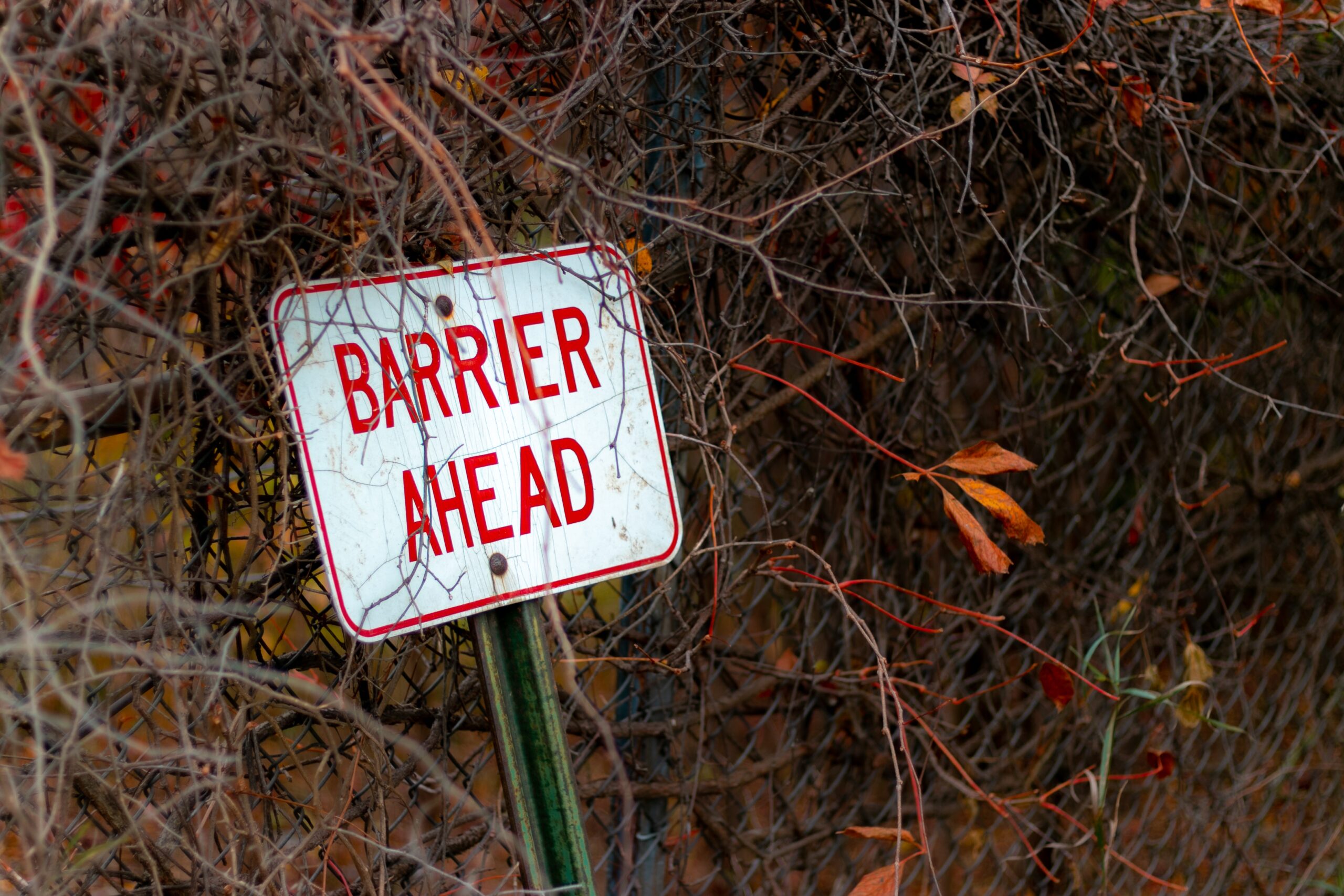 Selective focus shot of a barrier ahead sign leaned against a metal fence Selective focus shot of a barrier ahead sign leaned against a metal fence